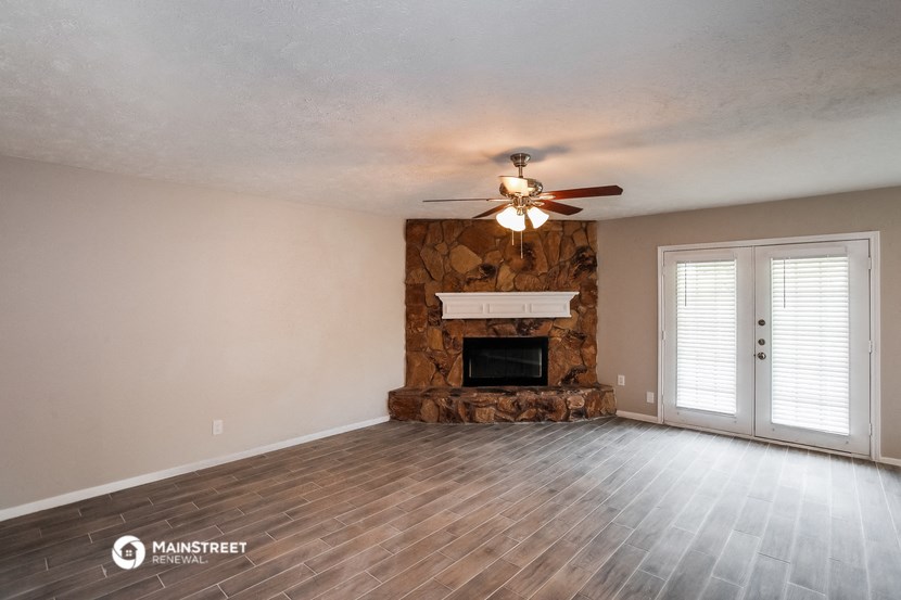 the living room with a stone fireplace and a ceiling fan