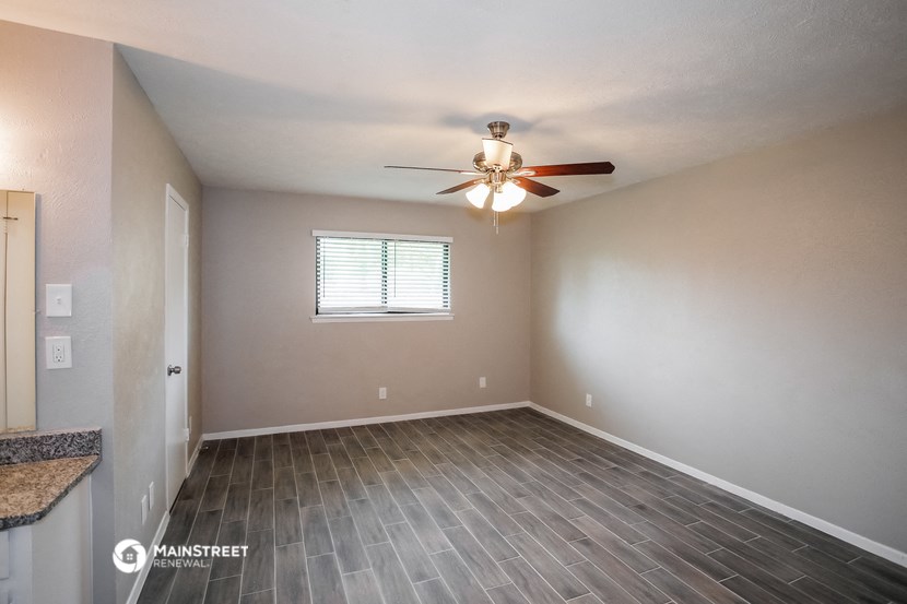 the spacious living room with wood flooring and a ceiling fan