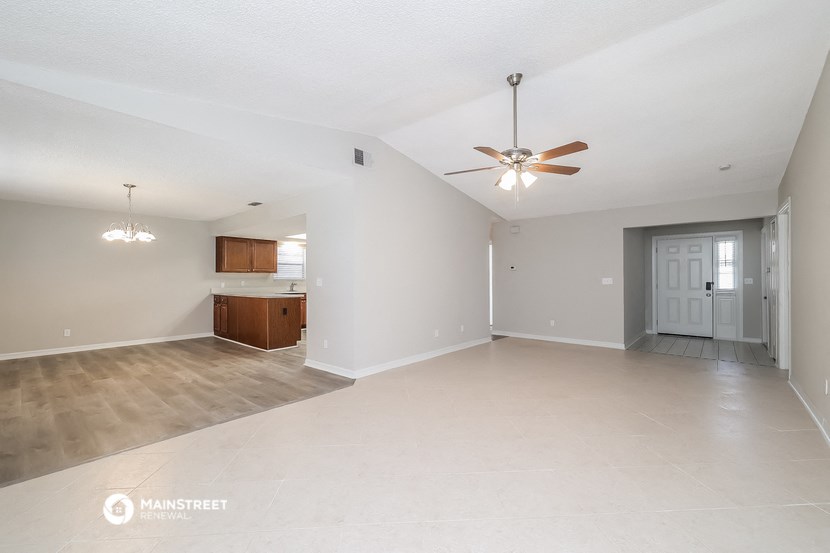 an empty living room with a ceiling fan and a kitchen