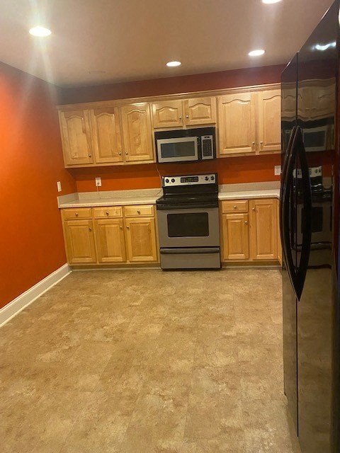 A kitchen with a black refrigerator, wooden cabinets, and a black stove top oven.