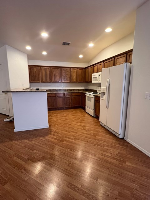 an empty kitchen with wood floors and white appliances