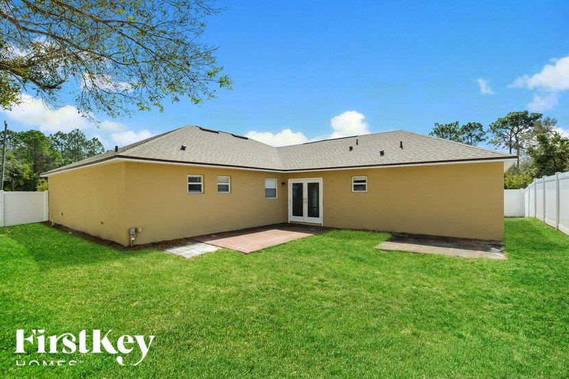 the backyard of a yellow house with a grass lawn and a white fence