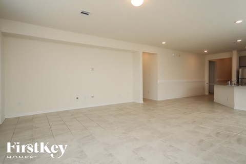 A spacious room with a tiled floor and a kitchen area in the background.