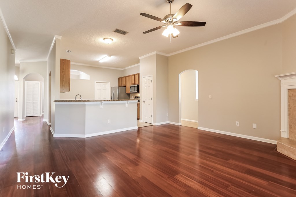 an empty living room and kitchen with wood flooring and a ceiling fan