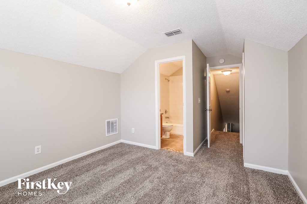 a spacious living room with carpet and a hallway to the bathroom