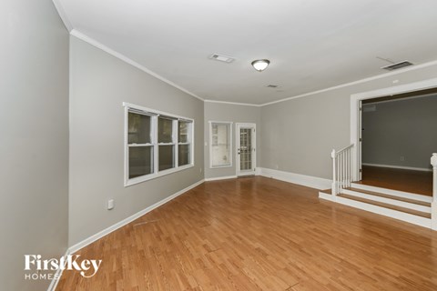 A spacious room with wooden floors and a staircase leading to another room.