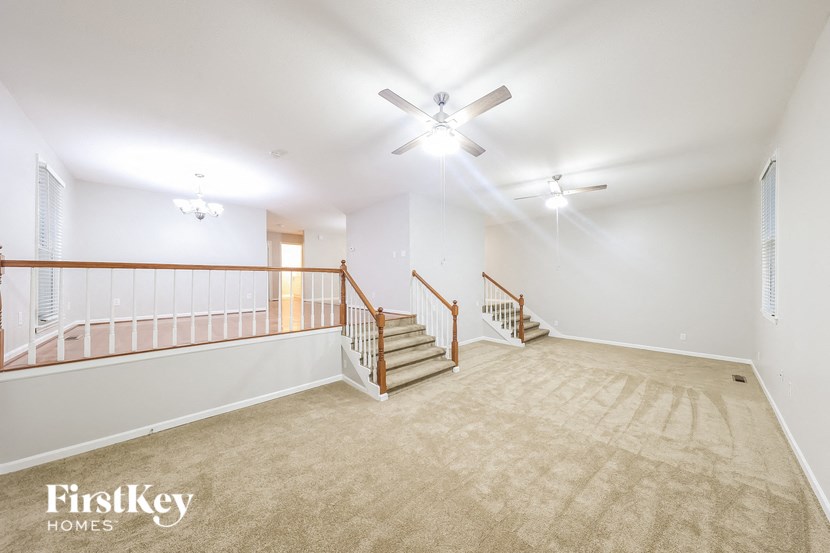 a spacious living room with carpeted stairs and a ceiling fan