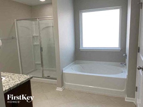 A white bathroom with a tub, shower, and a window.
