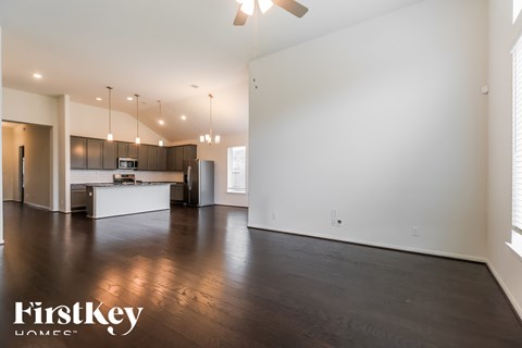 A spacious room with wooden floors and a kitchen area in the background.