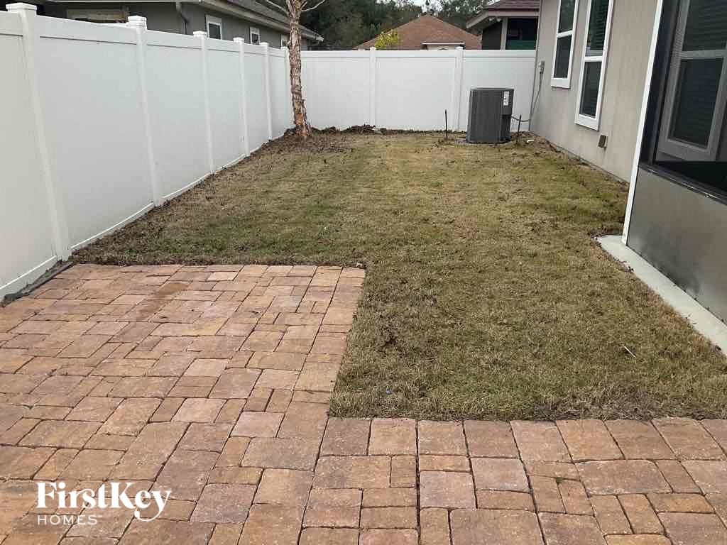 a backyard with a brick patio and a white fence