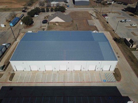 A large building with a blue roof is surrounded by a parking lot.