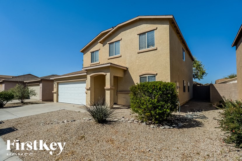 A beige house with a gravel driveway in front of it.