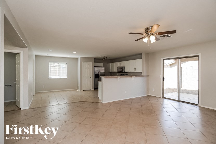 A spacious living room with a kitchen in the background and a ceiling fan above.