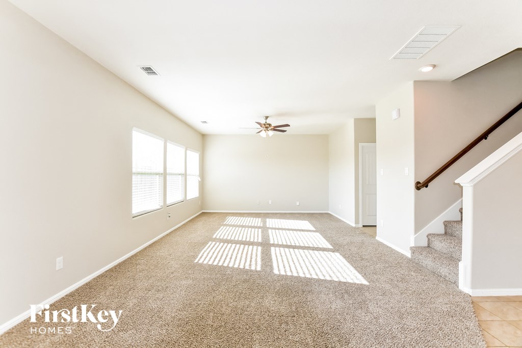 a carpeted living room with stairs and a ceiling fan