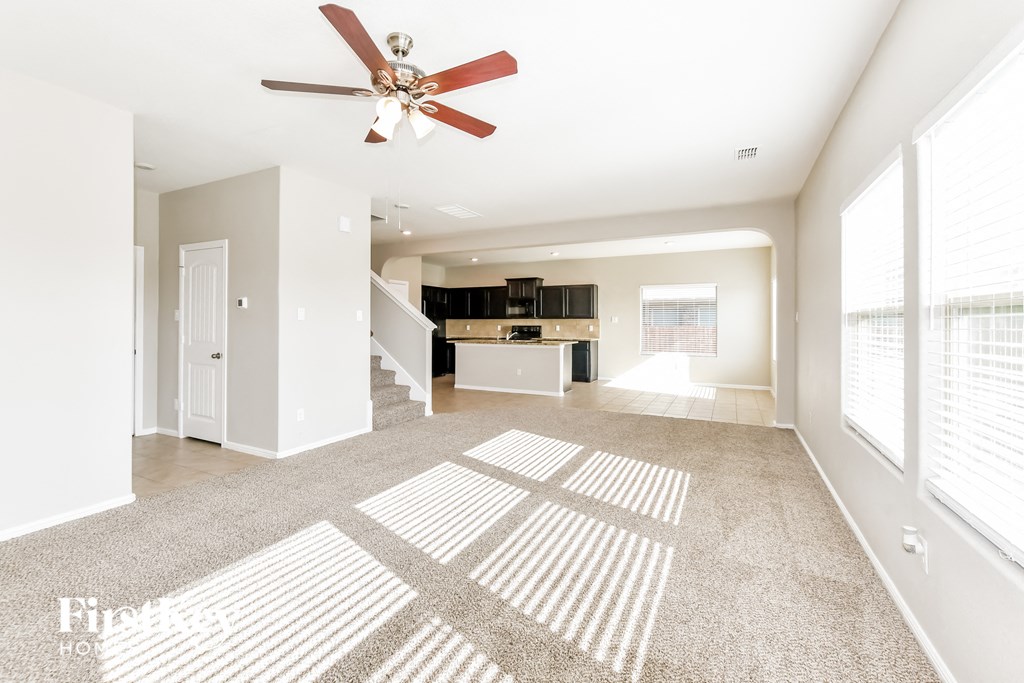 an empty living room with a ceiling fan and a kitchen