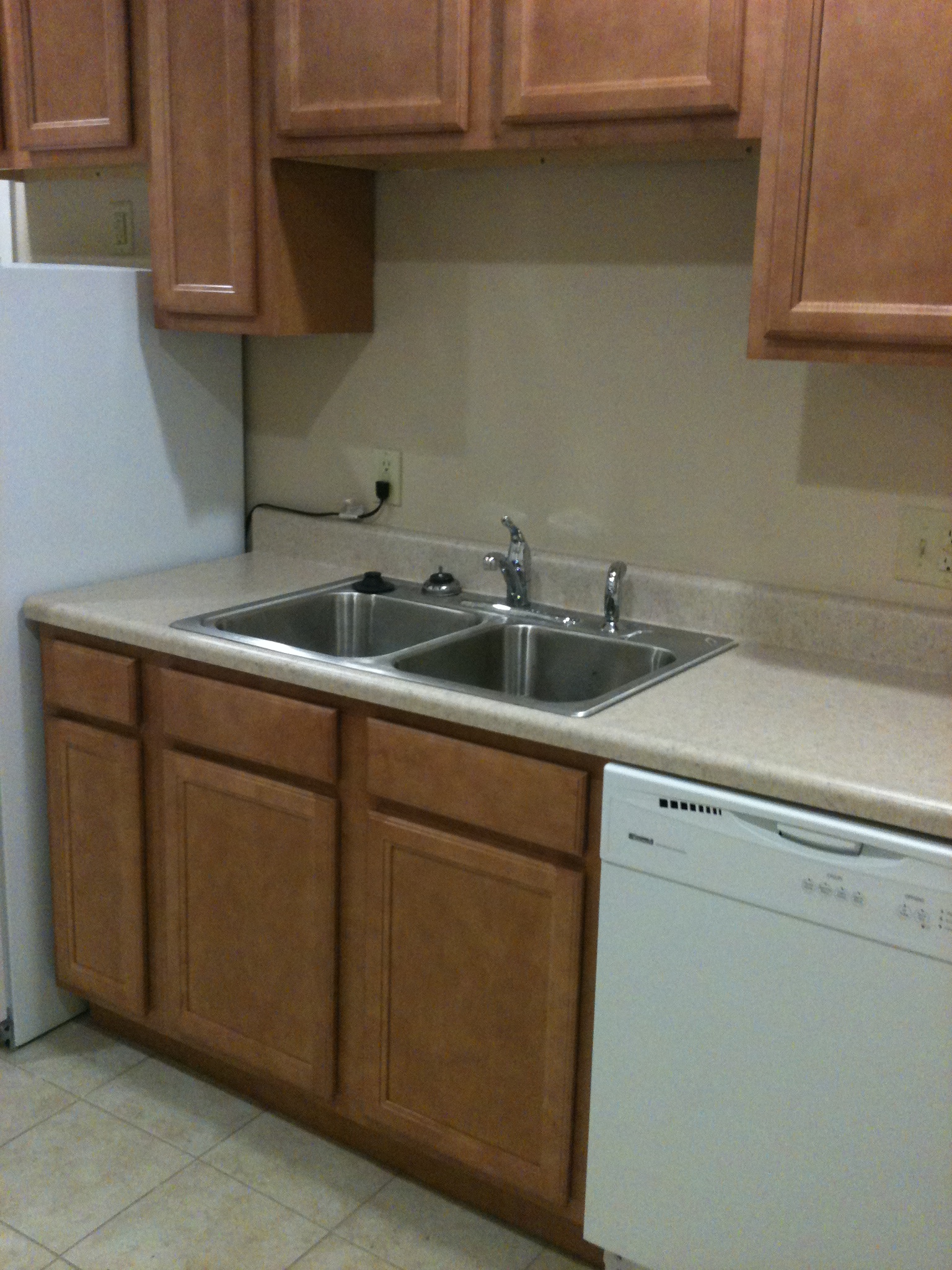 A kitchen with a white dishwasher and brown cabinets.