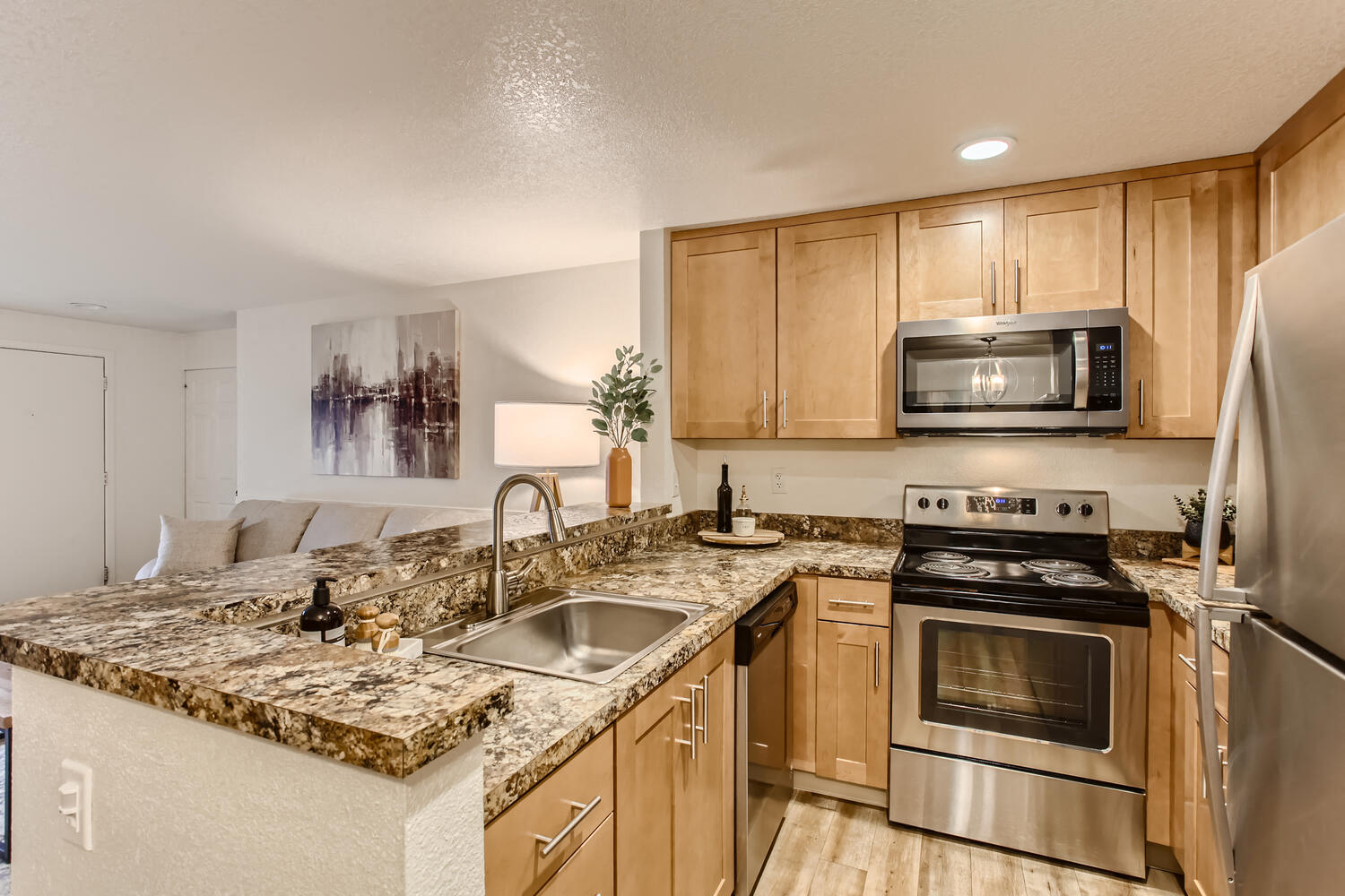 Pet Friendly Apartments in Lake Oswego OR - Westlake Meadows - Modern Kitchen with Granite Counters, Natural Tan Wood Cabinetry, Stainless Steel Appliances, Decorative Plants, and View of Living Area