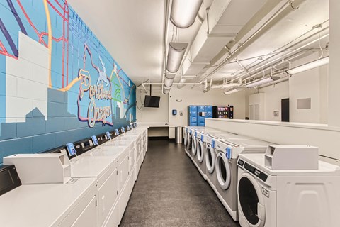 a laundromat with a row of washing machines and a wall with graffiti