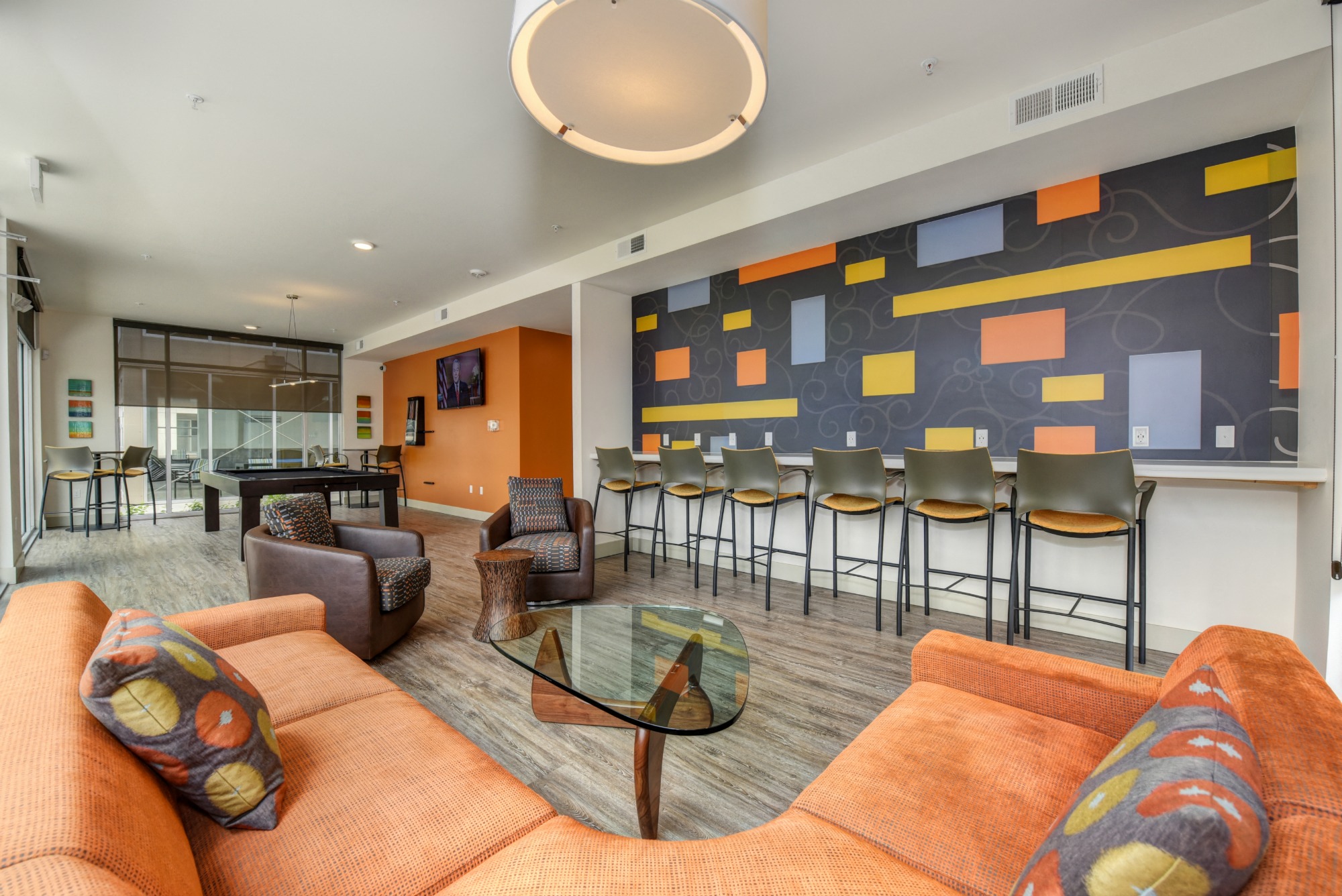 Community Clubhouse Lounge with Orange Sofas, Glass Table and Pool Table in the Distance