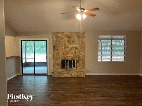 an empty living room with a stone fireplace and a ceiling fan