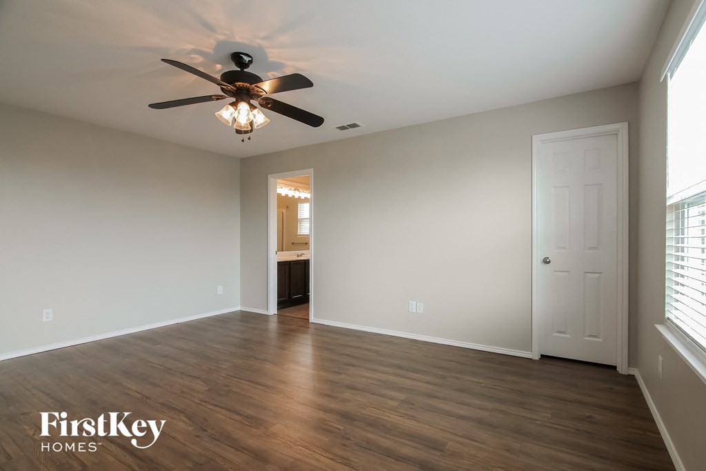 an empty living room with a ceiling fan and a door to a bathroom