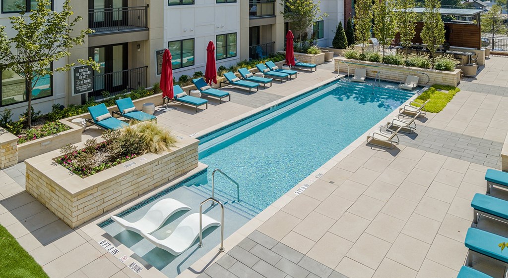 a swimming pool with lounge chairs and umbrellas in front of a building
