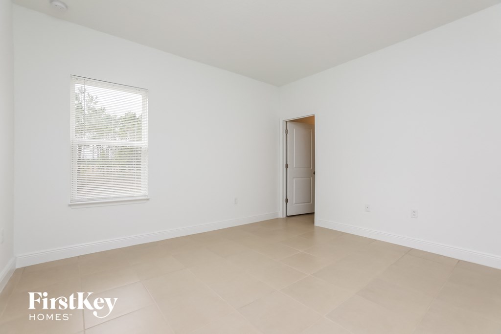 a spacious living room with white walls and tiled floors and a door