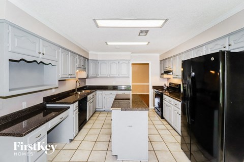 A kitchen with white cabinets and a black refrigerator.