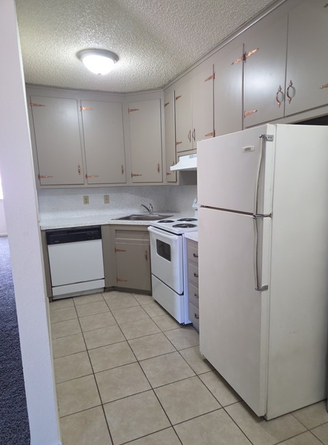 A white refrigerator stands in a kitchen with white cabinets.