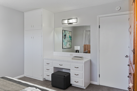 A white vanity with a mirror and a black ottoman is in a room.