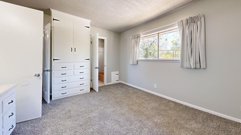 A room with a white cabinet and drawers, a window with curtains, and a carpeted floor.