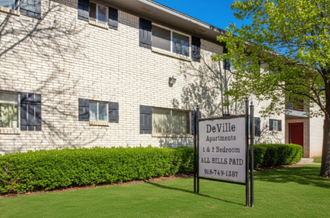 A sign for DeVille Apartments stands in front of a building.