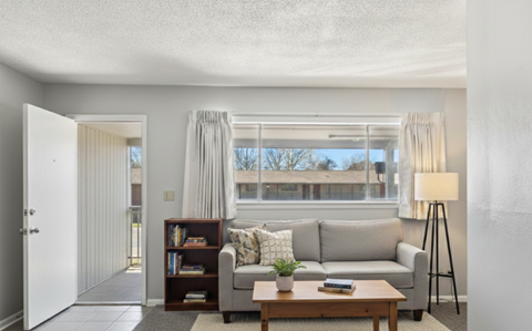 A living room with a grey couch, a wooden coffee table, a bookshelf, and a floor lamp.