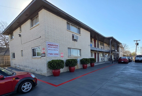 A red car is parked in front of a building with a sign that reads "Highview Apartments.".