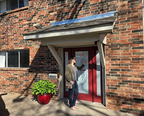 A woman stands in the doorway of a brick building.