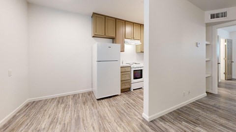 A kitchen with a white fridge, microwave, and oven with wooden cabinets and a wooden floor.