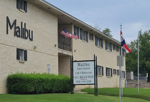 A building with the name Malibu on it and a sign in front that says Malibu Apartments 1 & 2 Bedroom.
