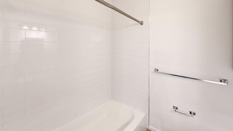 A white tiled bathroom with a white tub and a white shower door.