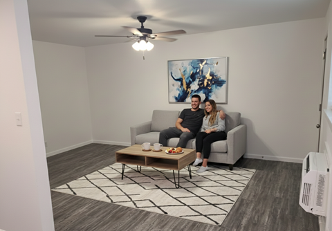 A man and woman are sitting on a couch in a living room with a painting on the wall and a coffee table in front of them.