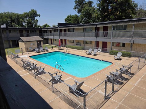 A pool surrounded by chairs and a fence.