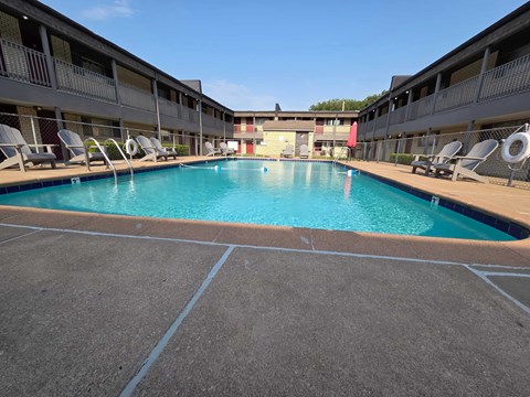 A large swimming pool in a courtyard surrounded by chairs.