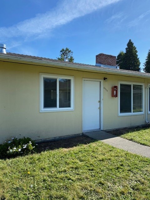A yellow house with a white door and a red fire extinguisher on the wall.