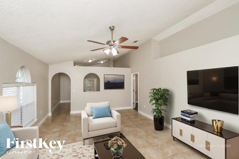 A living room with a white couch and a flat screen TV mounted on the wall.