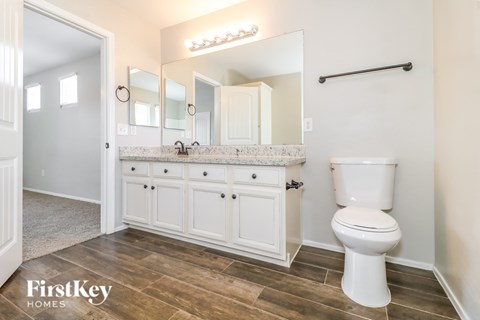 A white toilet sits in a bathroom with a wooden floor and a mirror above the sink.