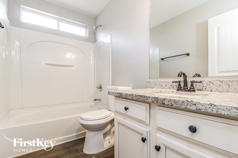 A white bathroom with a marble countertop and a large tub.