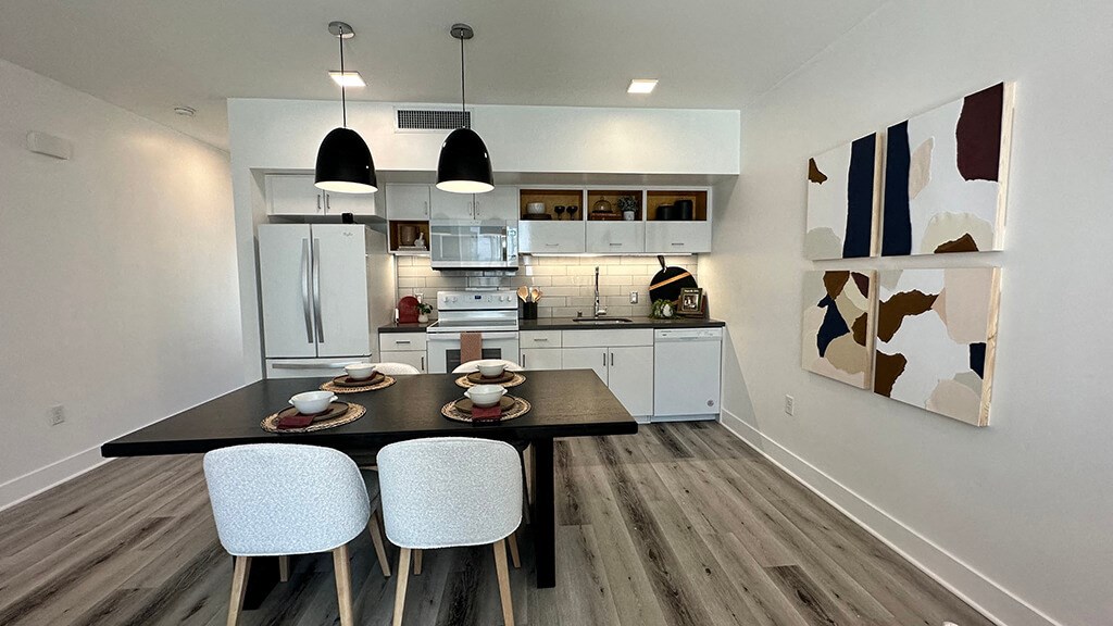 a kitchen with white cabinets and a black table with white chairs at Idea1 Apartments in San Diego CA