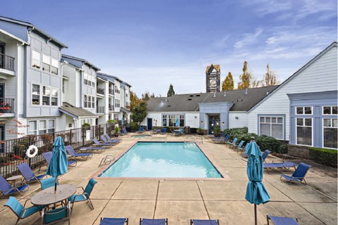 a swimming pool with blue chairs and umbrellas in front of apartment buildings