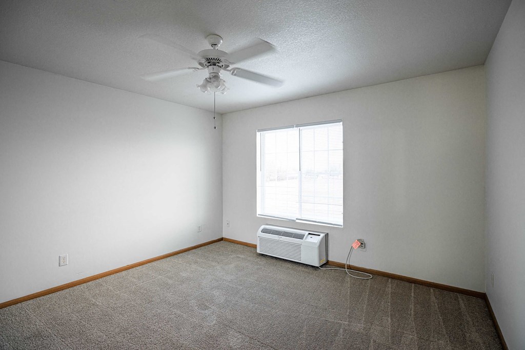 A room with a ceiling fan and a window with an air conditioner unit underneath it.