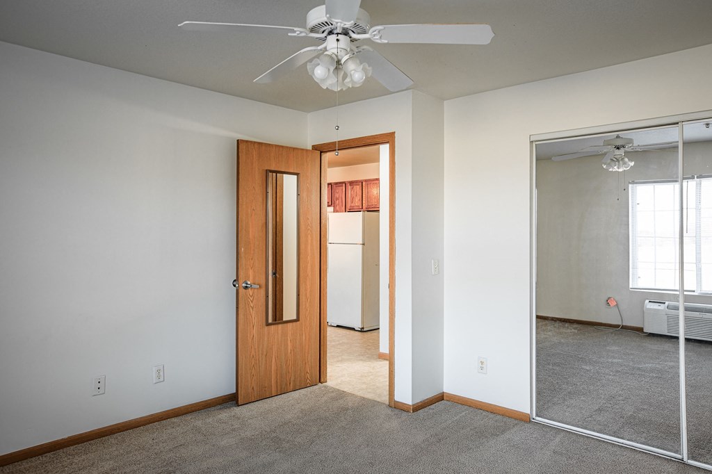 A room with a ceiling fan and a door leading to another room.