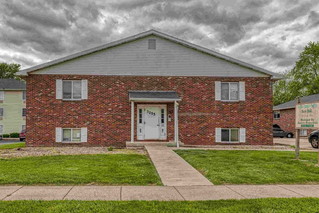 A red brick house with a white door and a sign on the lawn.